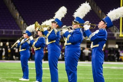 A marching band performs on the field of a football stadium.