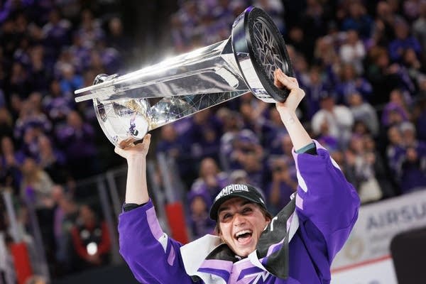 A hockey player holds a trophy above her head.