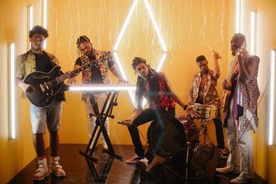 Five musicians in a room pose with their instruments