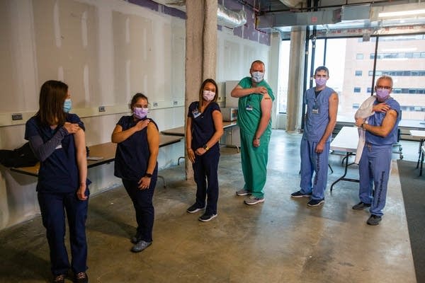 6 people pull up their sleeves to show bandages.