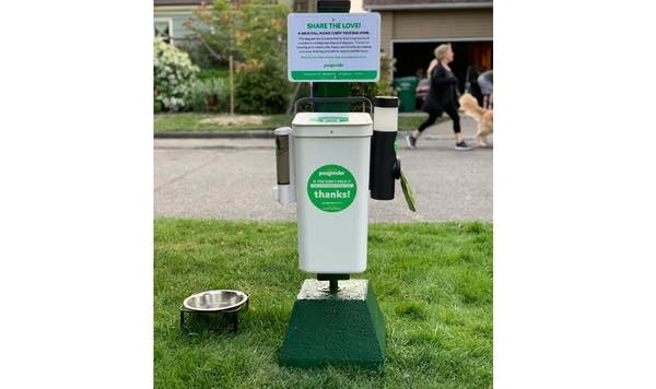 Photo of a "PooGooder" garbage bin for dog poop, outside on green lawn