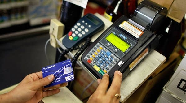 A woman uses a credit card reader to charge a credit card from a customer for payment at Lorenzo's Italian Market in Miami, Fla.