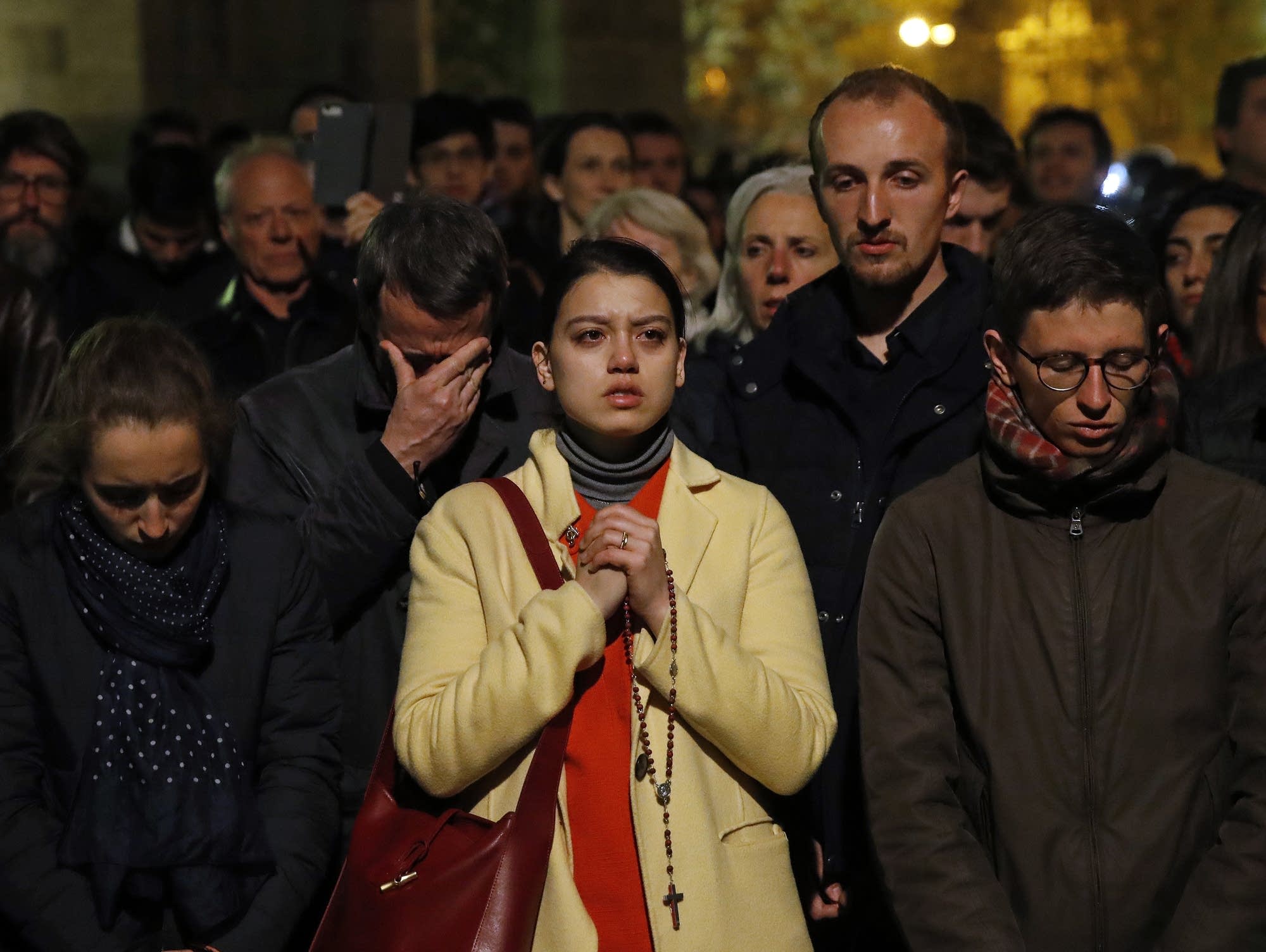 People pray as Notre Dame cathedral burns in Paris Monday, April 15, 2019.