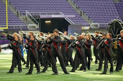 A marching band performs on the field of a football stadium.