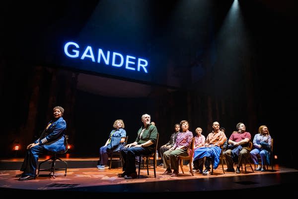 A group of performers sit in seats under a sign that reads 