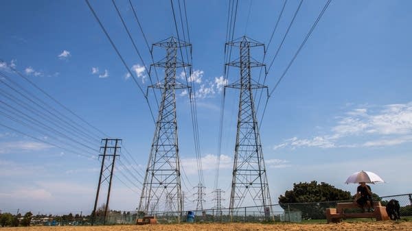 A man sits under his umbrella under high tension power lines in California in August 2020, two days after the state ordered rolling power outages.