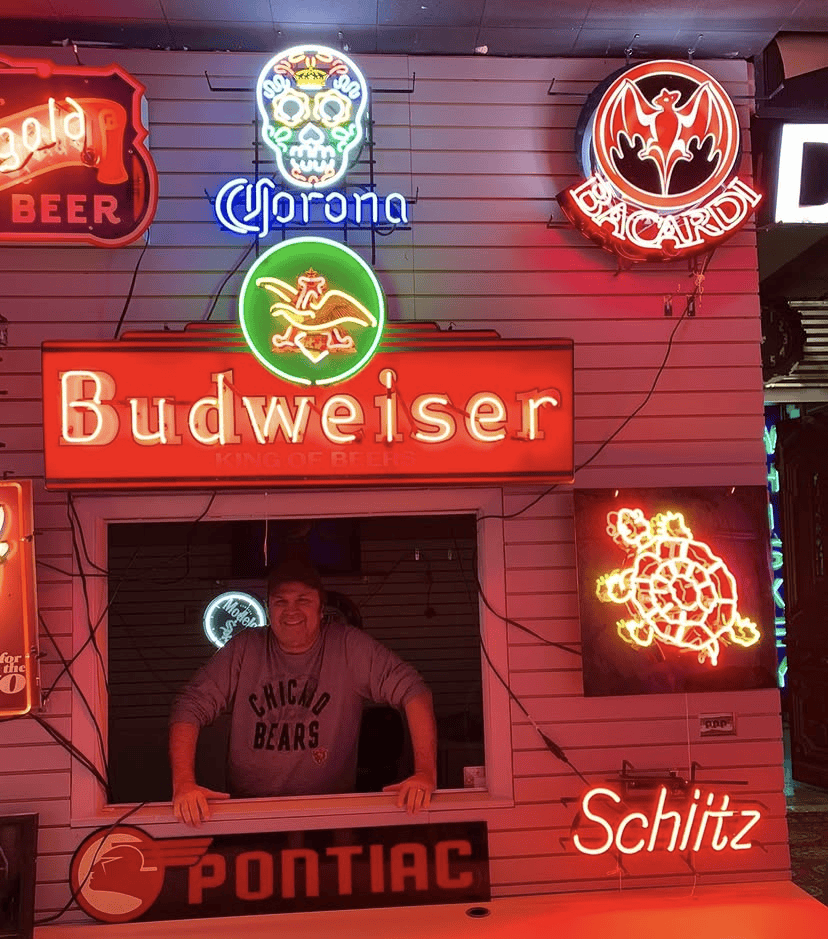 A man stands behind a desk surrounded by neon signs