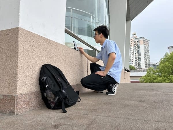 A graduate kneels in a quiet corner for an online interview in Shanghai.