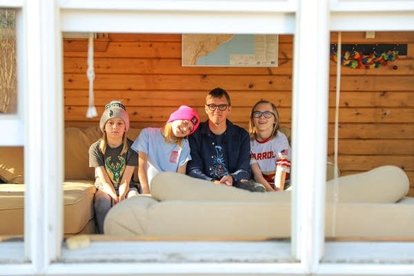 A man and four children photographed through a window on a porch. 