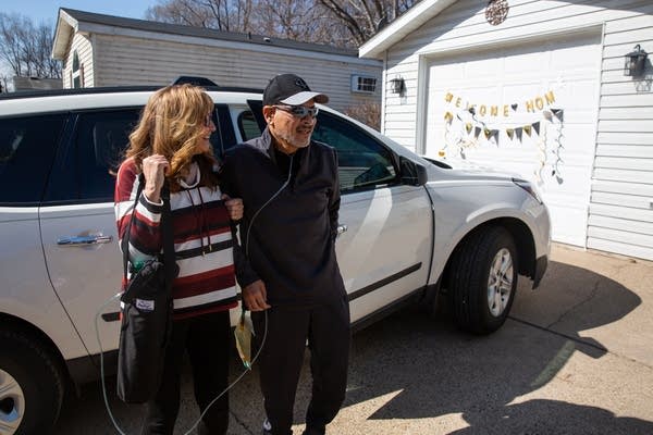 Two people walk from a car into a home.