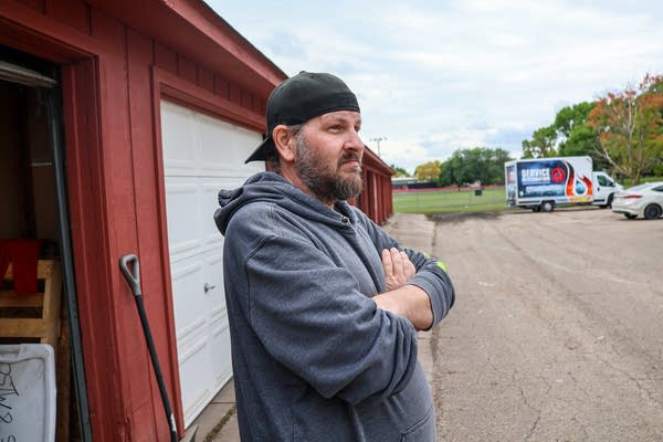A man poses for a photo with his arms crossed in front of a garage.