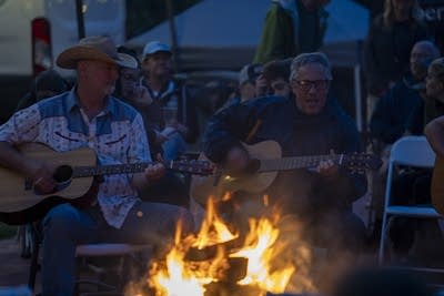 a crowd of people playing music around a campfire 