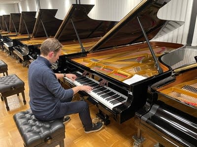 A pianist plays a piano in a vast showroom filled with pianos