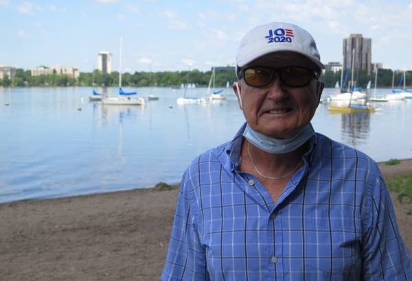 A man in a hat stands in front of a lake. 