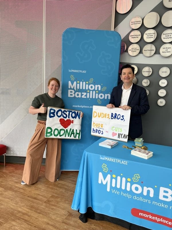 Million Bazillion hosts standing next to each other holding two signs made by a fan