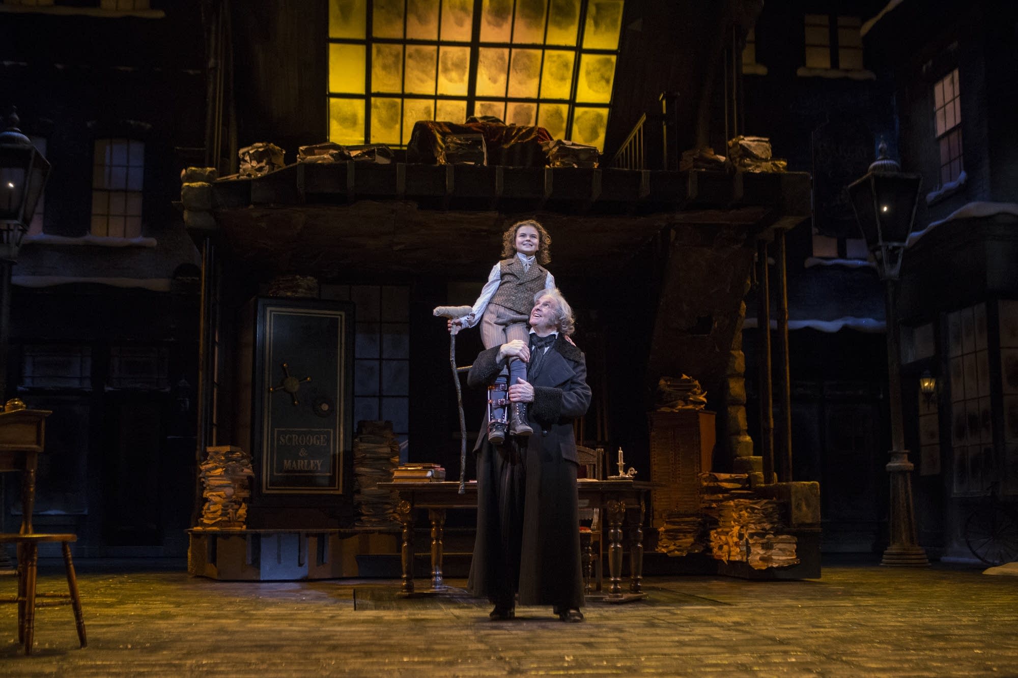 Ebenezer Scrooge lifts Tiny Tim during the closing scene.