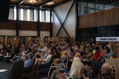 A crowd sits and listens in a large library setting.