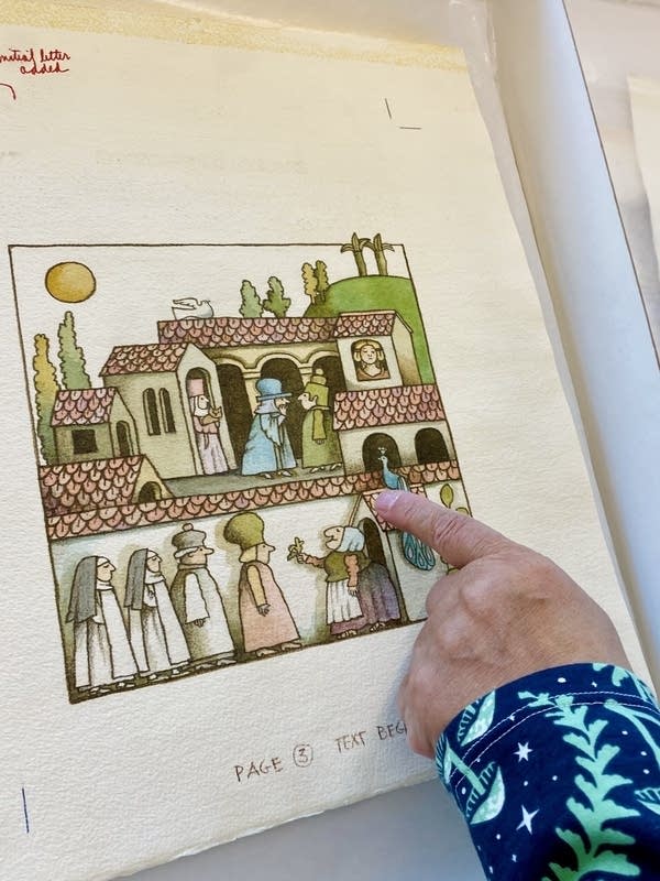 A woman gestures to a set of drawings preserved in a library.