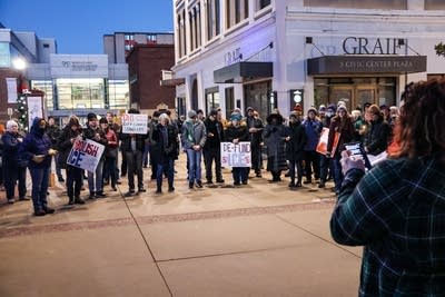 A group of people stands in a large circle while a woman speaks into a bullhorn.