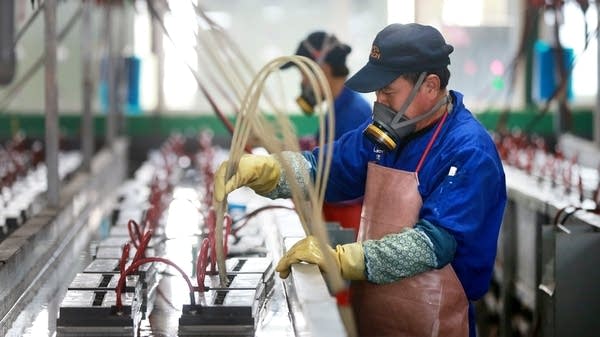 A masked factory worker works on a machine line. 