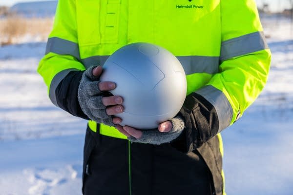 Close-up of a man holding a metal, spherical sensor.