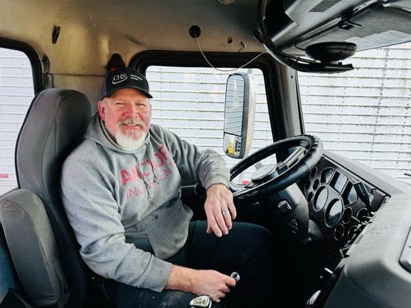 A man smiles for a photo inside the cab of his semi truck.