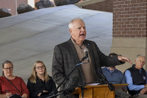 A man in a dark gray suit jacket speaks emphatically at a podium.