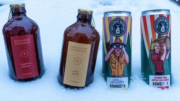 Two glass bottles of kombucha next to two cans of kombucha.