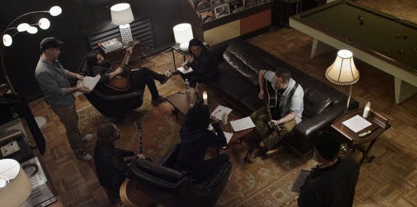 Seven people gathered in a lounge working out musical arrangements