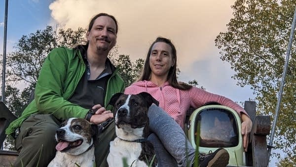 A man and woman pose for a photo with their two dogs outside.