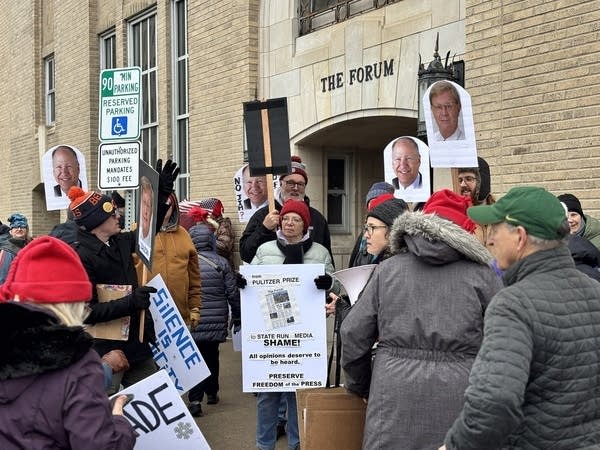 A group of protesters gathers on the sidewalk outside the entrance to the Fargo Forum.