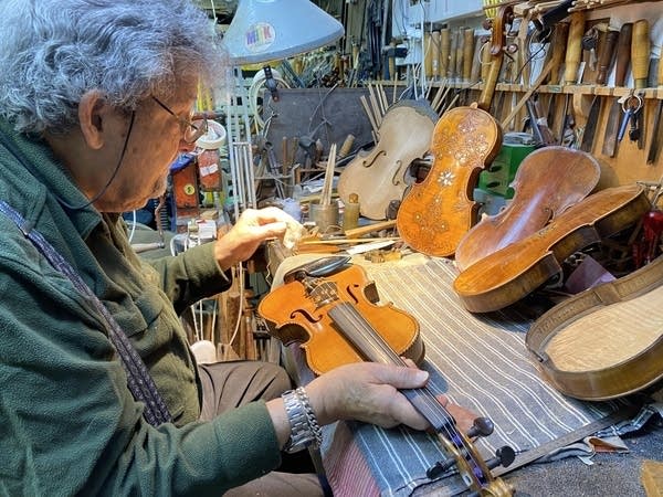 A man works inside a workshop with a collection of violins.