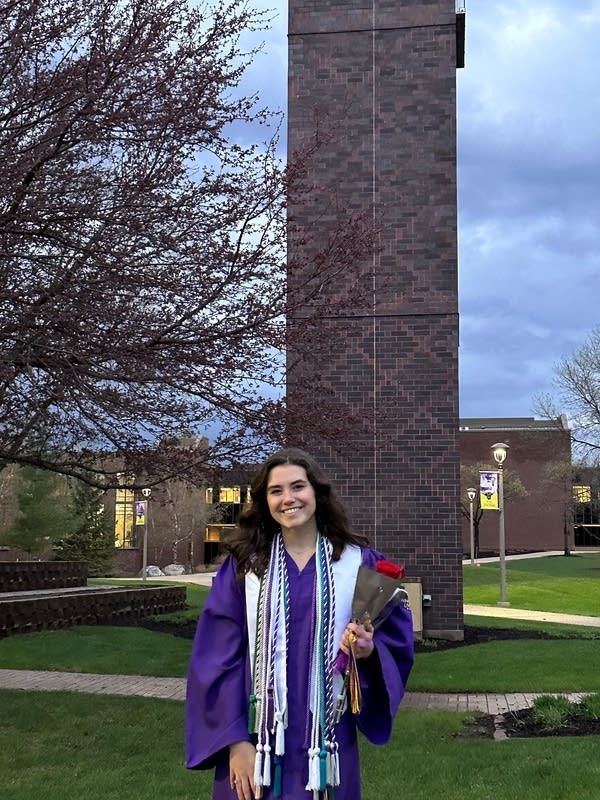 A woman wearing a purple graduation gown stands on a college campus