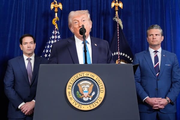 President Donald Trump speaks at a press conference, flanked by Marco Rubio (left) and Pete Hegseth (right).