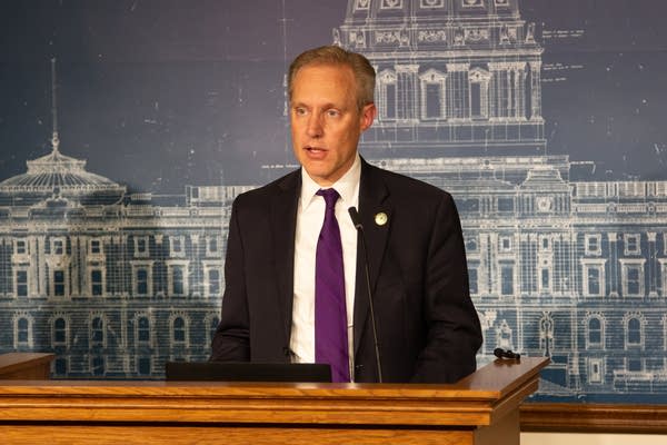 A man in a suit speaks at a podium.