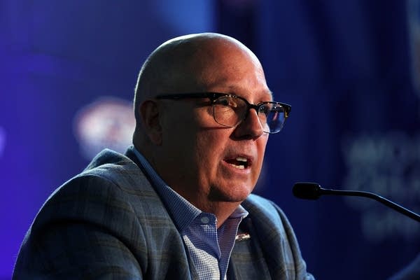 A man in a suit speaks into a microphone.