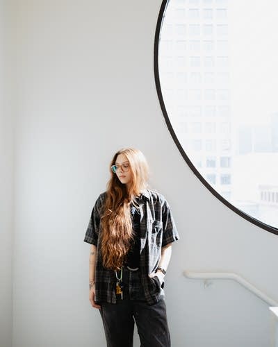 Runo Plum wears a button-down shirt over a T-shirt, jeans, and boots.