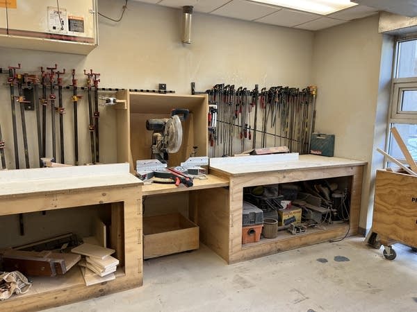 Part of the woodshop at MakerSpace NYC. Tools hang from the walls. There's a saw in the middle of two tables.