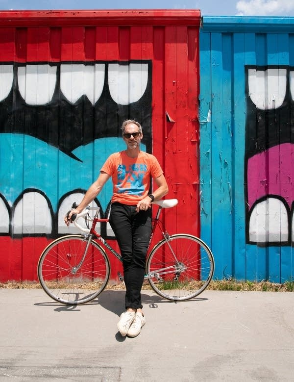 A man in sunglasses stands next to a bicycle on a sunny day