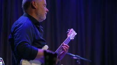 A musician plays guitar onstage in a music venue