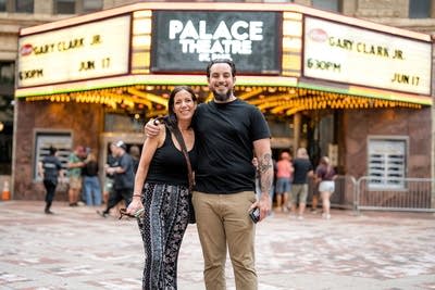 Two music fans pose for a portrait outside a large music venue