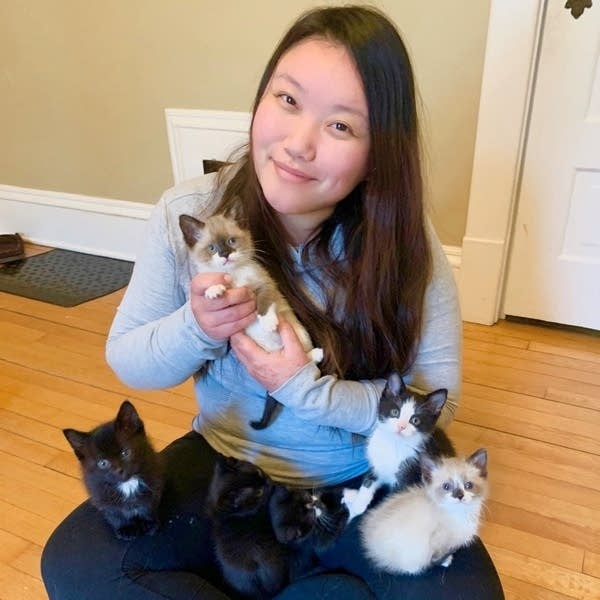 A woman holds kittens while sitting on the floor.