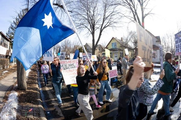 A woman holds a Minnesota state flag while marching with a crowd of protesters.
