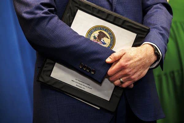 Close-up of a man holding a binder with the U.S. Department of Justice seal on the front.