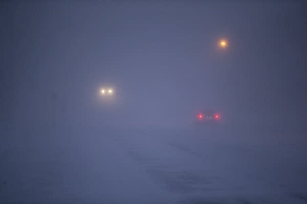 Cars are barely visible driving in the snow. 