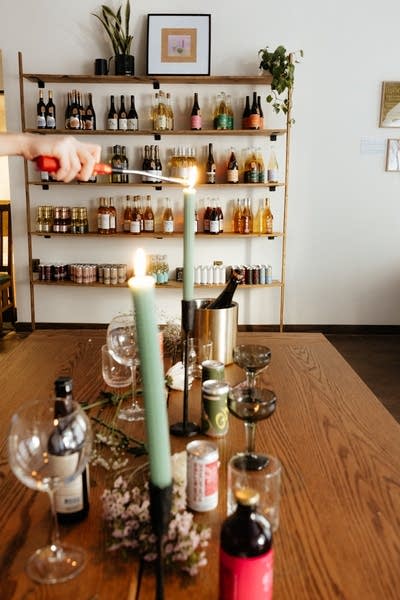 Candles are lit at a table inside a store. Many bottles are on display.