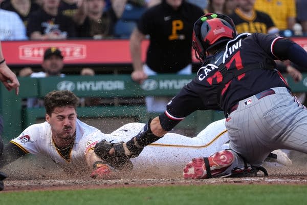 Dust flies as a baseball runner slides on his stomach into home plate, barely missing the glove of the catcher.