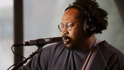 A musician sings and plays guitar in a recording studio