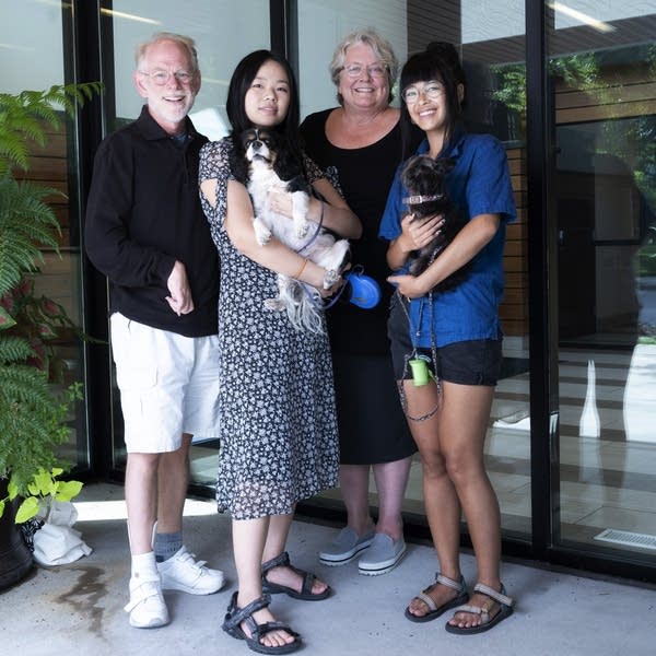 A family of four poses for a photo. Two girls are holding small dogs.