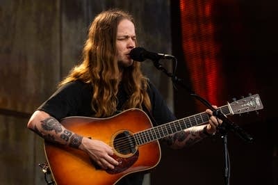 A musician sings and plays flatpick guitar on a large outdoor stage